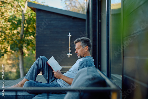 Bild auf Leinwand Mature man reading on a modern patio sofa, enjoying peaceful solo time outdoors