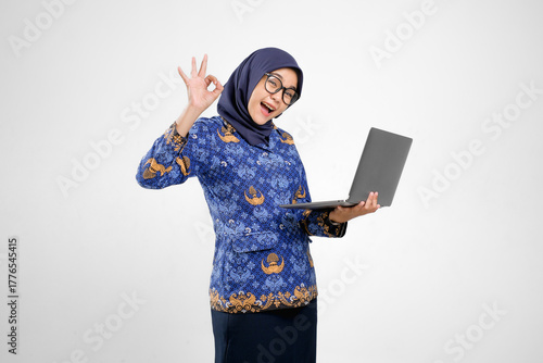 Fotografía PNS indonesia, ASN Indonesia, Guru Indonesia in korpri uniform showing OK hand sign while holding laptop, concept of success, positivity, and digital education