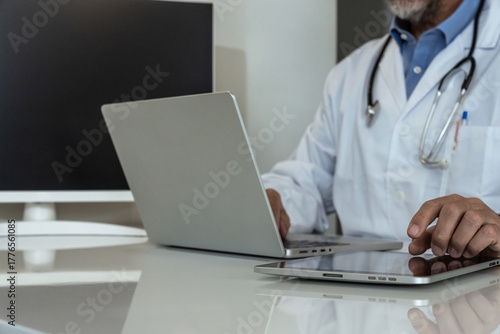 Dedicated doctor in a clinic setting, working with a tablet and laptop, symbolizing modern medical practice