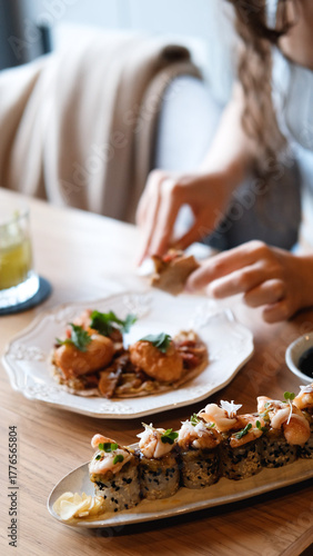 A beautiful girl eats Japanese sushi rolls with chopsticks, smiling with pleasure