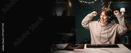 E-sport female gamer in headphones play online video game doing winner gesture celebrate clenching fists while using computer. Young gaming player broadcast live streaming plays video games