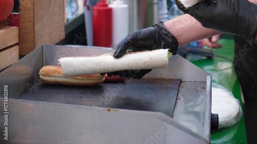 Close-up of street cafe worker's hands in black gloves flipping a filled wrap roll on griddle during doner kebab fast food preparation service