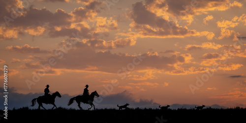 Cowboys riding quarter horses at sunset with dogs herding a horse herd in a quiet western landscape