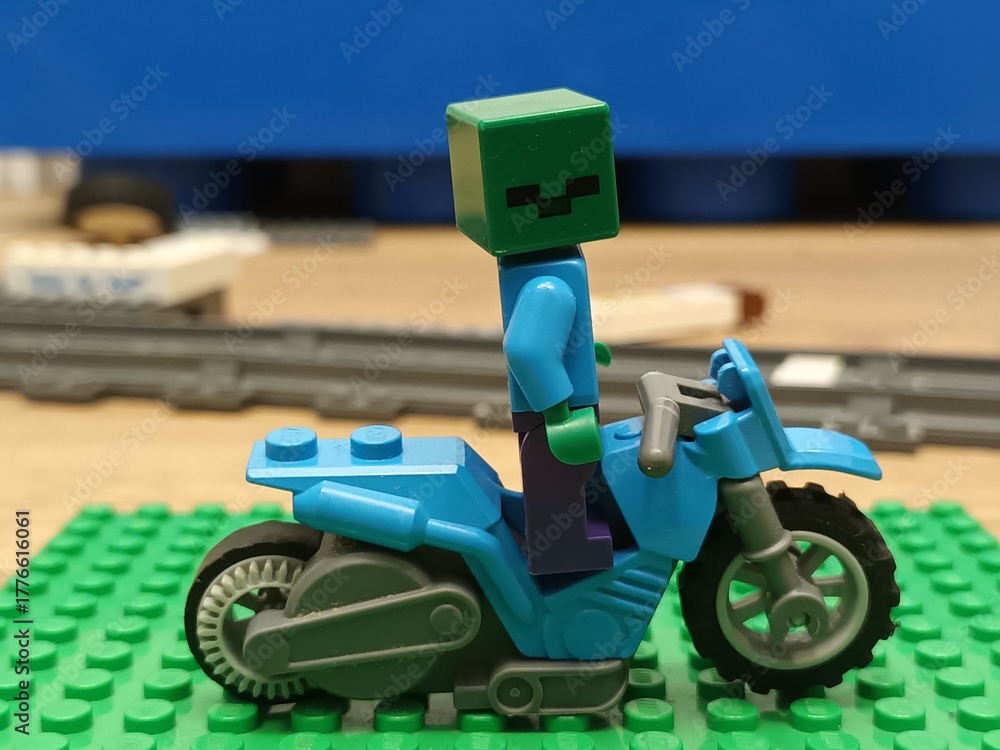 Naklejka premium A LEGO Minecraft zombie character figure riding a blue LEGO motorcycle, placed on a green baseplate