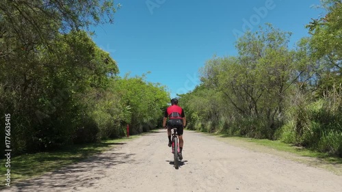 Male cyclist training outdoor. Aerial view, drone following, tracking shot. Cyclist riding a Mountain Bike MTB through a city natural reserve / park. Gravel biking concept. Cyclist red cycling jersey.