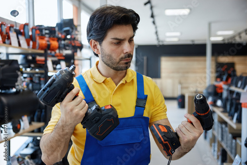 A man worker is holding impact and power drills in his hands in a store
