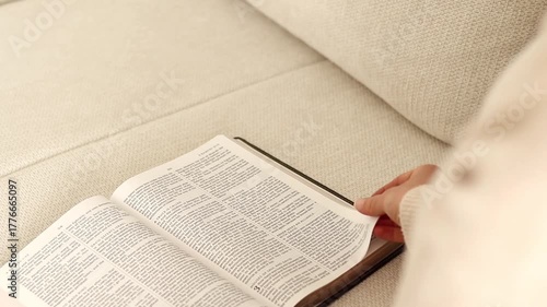 Christian woman is reading and studying from holy bible book while sitting on sofa at home. Biblical concept.