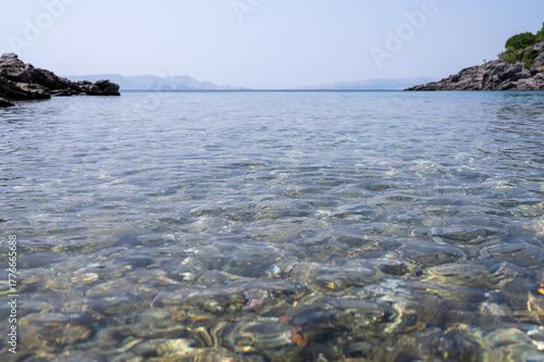 Fototapeta Naklejka Na Ścianę i Meble -  View of stones in the  water at the seashore with island in the background