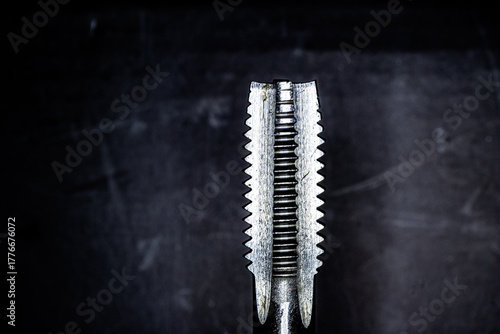 Close-up view of a metal thread tap showing detailed cutting edges and grooves. The precision tool is used for creating internal threads in metalworking and engineering applications.
