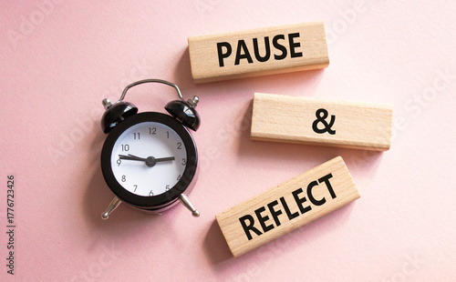 Pause and Reflect symbol. Concept words Pause and Reflect on wooden blocks. Beautiful pink background with alarm clock. Business and Pause and Reflect concept. Copy space.