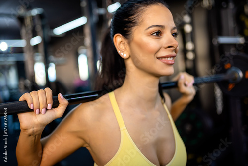 Behang Young woman doing weighted squat on smith machine