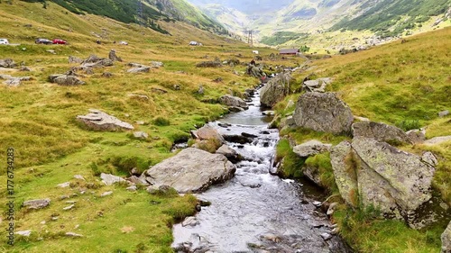 Flight over the narrow turbulent river flowing by the rocks. Some people take pictures on the boulders. The Carpathian Mountains, Romania.