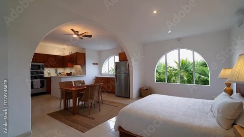 A well-appointed hotel room with a bed, dining area, and kitchenette overlooks lush greenery.