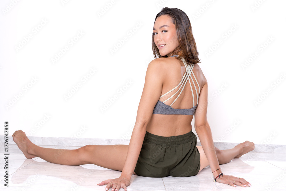 Fototapeta premium Woman performing seated split stretch on white floor, flexibility and wellness routine.