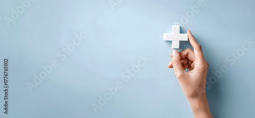 A human hand holding or reaching for a white medical cross symbol on a solid blue background