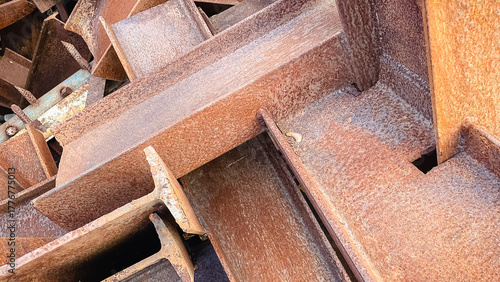 Close-up of a chaotic pile of heavily rusted metal I-beams, creating an industrial abstract background texture