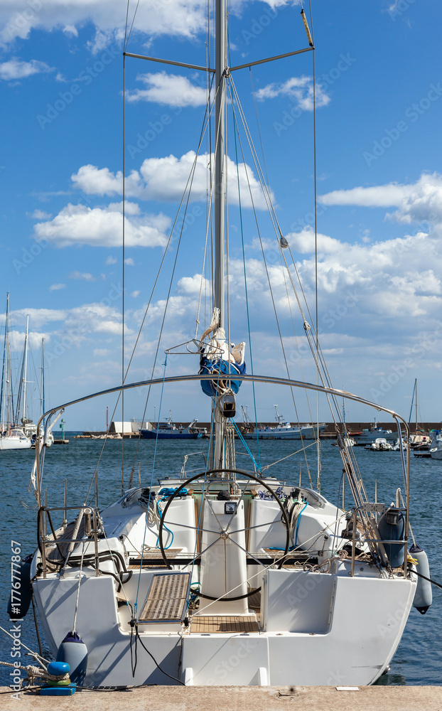 Obraz premium A sailboat moored at the picturesque La Caletta Port in Sardinia, Italy, with a clear blue sky and calm sea.