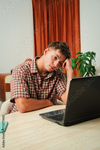 A young man displays visible frustration while working on a laptop, showing signs of stress and confusion as he contemplates a problem that is clearly bothering him. He appears deep in thought.