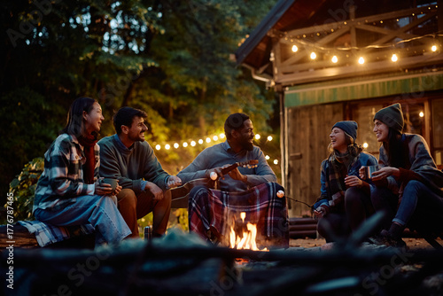 Fotografía Multiracial group of happy friends having fun while gathering around campfire in autumn