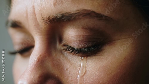 Close up of a woman’s face crying with an emotional tear rolling down her cheek showing a moment of sadness and vulnerability.