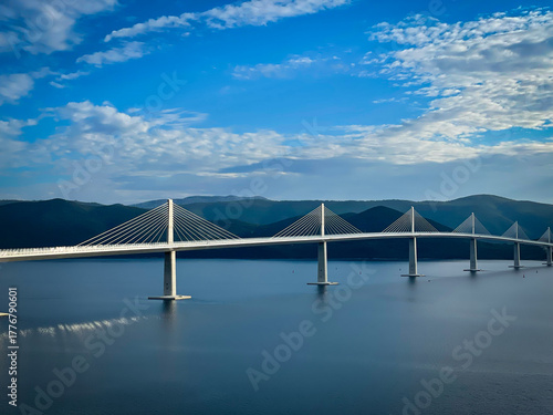 Elegant Peljesac Bridge rising over calm blue Adriatic waters with mountainous terrain in the background. Modern design and clear light highlight architectural and natural beauty in southern Croatia.
