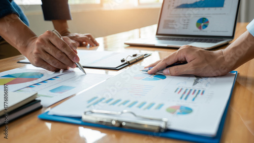 Business team collaborating over charts and reports, reviewing financial data on paper and laptop, discussing strategy, planning and analysis during a professional office meeting