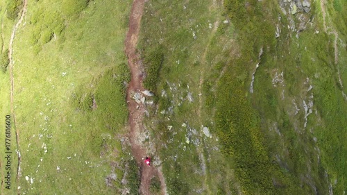 Beautiful mountain landscape. High-mountain massif, clouds over mountain peaks. Traveler goes to the top of the mountain, the figure of a man in red, aerial video shooting .