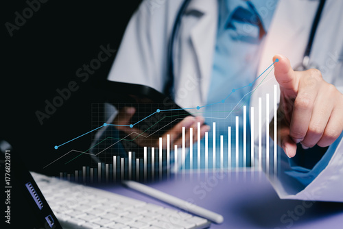 Healthcare professional analyzing data with graph on digital screen and laptop in modern office environment