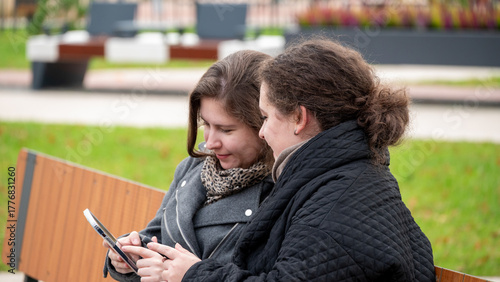 Two Friends Enjoying a Moment Together While Checking Their Phones on a Park Bench in Autumn