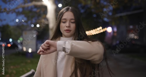 A woman walks at the night city street and look time on her hand, slow motion