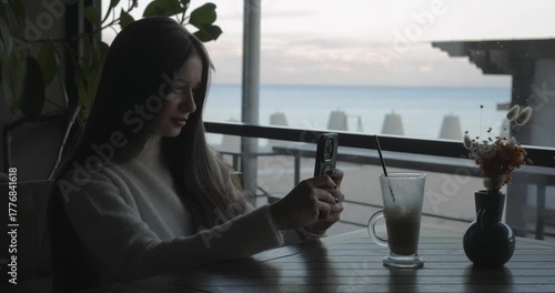 A woman takes a photo of a latte on her phone while sitting in a cafe