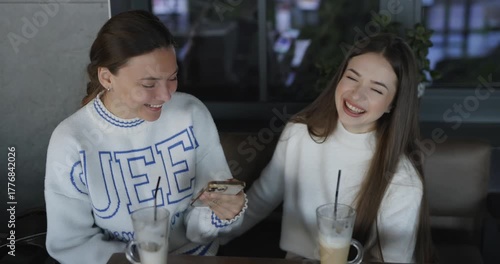 Women friends talking in cafe and laughing looking into smartphone, slow motion