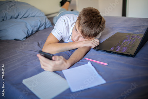 Foto Bored teenage boy lying on his bed, procrastinating homework by scrolling on his