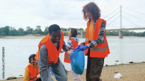 Group of volunteers cleaning river bank collecting plastic waste together.