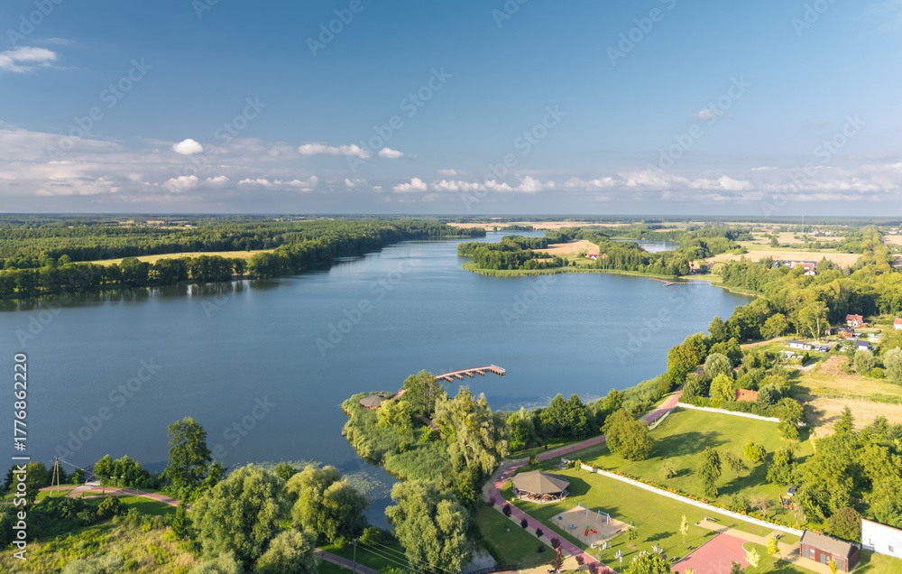 Obraz premium Aerial view of Wielgie Lake in Dobiegniew, Poland—expansive water with forested shoreline, docks, and lush rural landscape on a sunny summer day