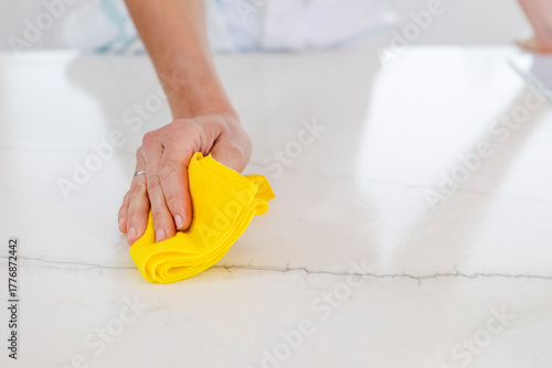 Foto Hand wiping kitchen counter surface with yellow cloth, cleaning and sanitizing h