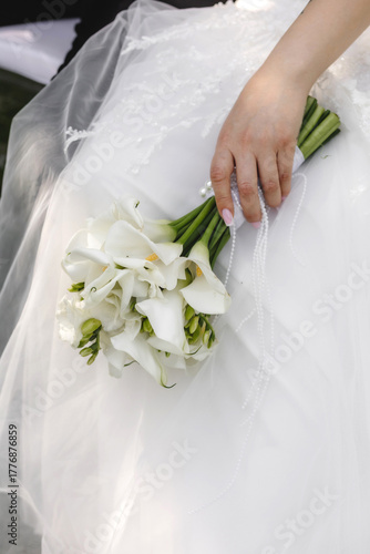 close-up, the bride holds a bouquet of flowers in her hand against the background of a wedding dress