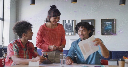 Collaborating three colleagues reviewing printed documents in meeting room, with tablet and coffee