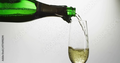 Green champagne bottle tilting and pouring champagne, filling flute, bubbles rising, flow slowing