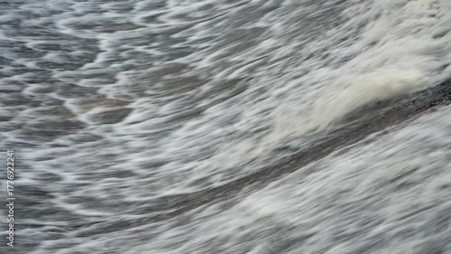 A fast-moving stream crashes down a rocky cascade in a close-up view, forming white foam and textured splashes that highlight nature’s raw energy.