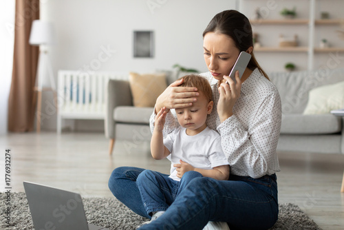 Картината върху платно A worried mother sits on the floor with her young child who has a fever