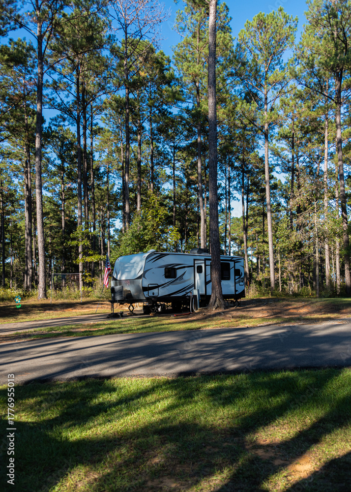 Obraz premium A trailer is parked in a scenic forest campground surrounded by tall pine trees. The peaceful setting suggests a perfect escape in nature.
