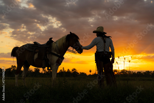 Silhouette of a cowboy standing beside his horse in the golden light of sunset on the western plains. Peaceful and cinematic moment capturing freedom and western lifestyle.