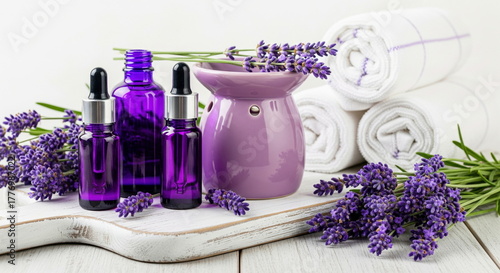 Lavender essential oil bottles, fresh lavender flowers, an aroma diffuser, and rolled towels for a relaxing spa and aromatherapy concept.