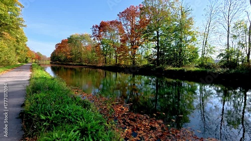 Colorful foliage mirrors tranquil water, Peaceful lakeside pathway surrounded by vividly colored autumn leaves