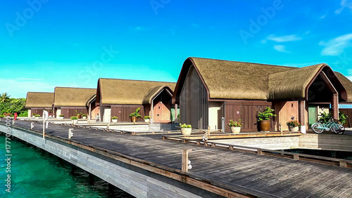Foto Row of luxurious overwater bungalows with thatched roofs, connected by a long wo