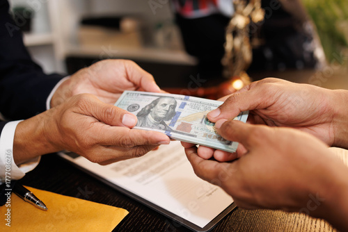 A man is handing a stack of money to another man. The man receiving the money is wearing a suit and tie. The scene appears to be a business transaction or negotiation

