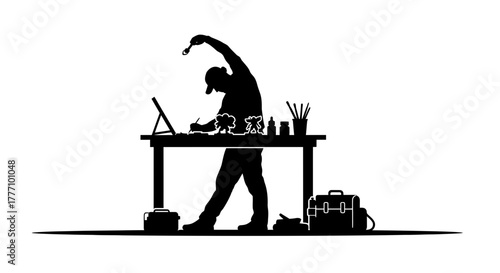 Artist in silhouette stretching while working at a desk with digital tablet and art supplies, symbolizing creativity and dedication