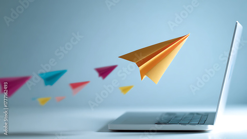 Paper airplanes flying out of a laptop screen on a light blue background in a studio shot