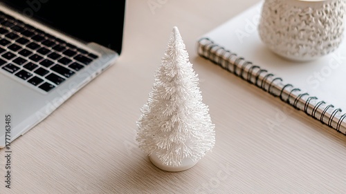 Close up of a white christmas tree decoration next to a laptop and notebook on a wooden table